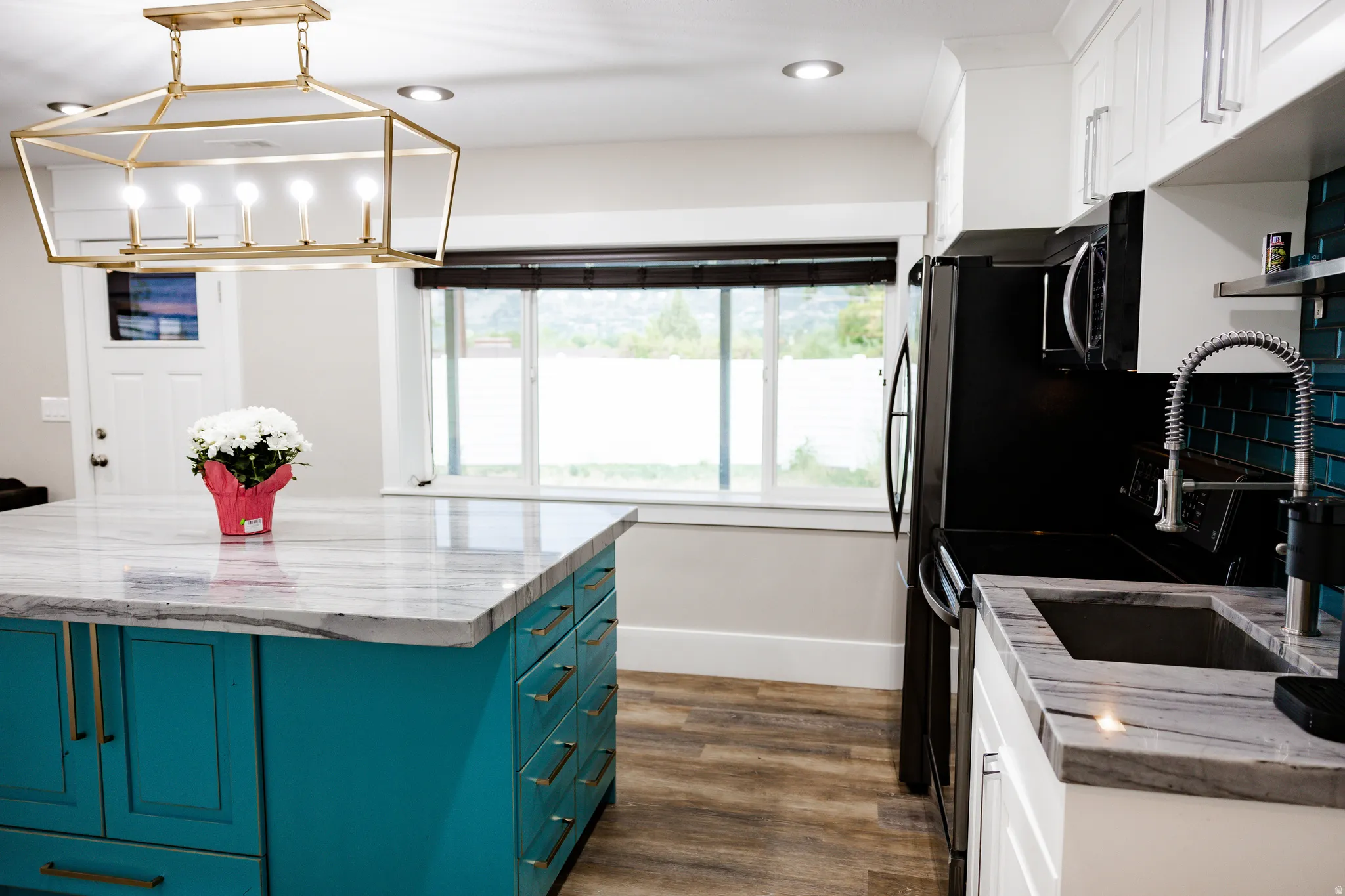 Basement Contemporary kitchen featuring a teal-finished island with brass hardware and a white quartz countertop, stainless steel appliances including a double-wall oven and under-mount sink, white cabinetry with brushed nickel fixtures, wood-finish floor