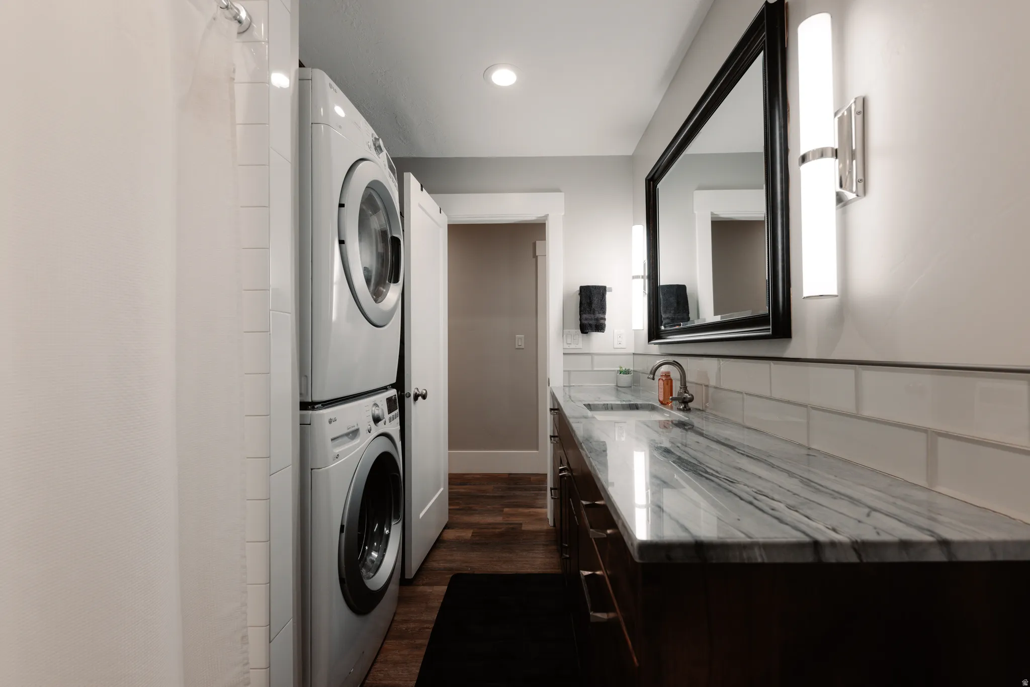 Dedicated laundry room featuring stacked front-load washers and dryers with polished stainless steel finishes