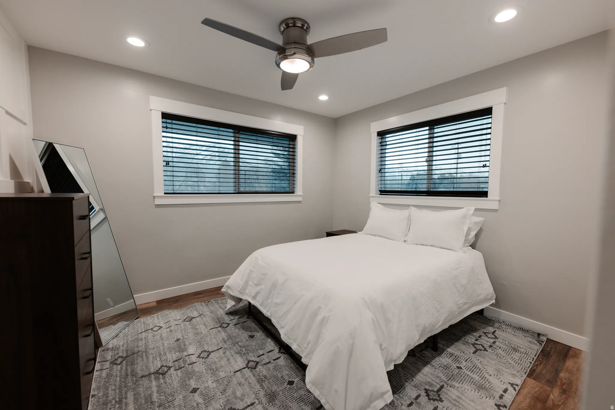 Recessed ceiling lighting, wood-finish flooring, two windows with blinds, and a ceiling fan with integrated light