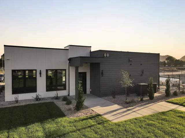 Modern architectural design featuring a clean-lined facade with mixed material finishes—white and charcoal exterior cladding—complemented by expansive black-framed windows and glass doors