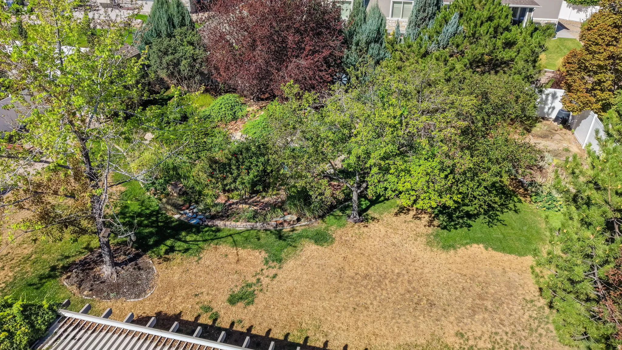 Expansive property featuring mature trees, diverse plantings, and a stone retaining wall