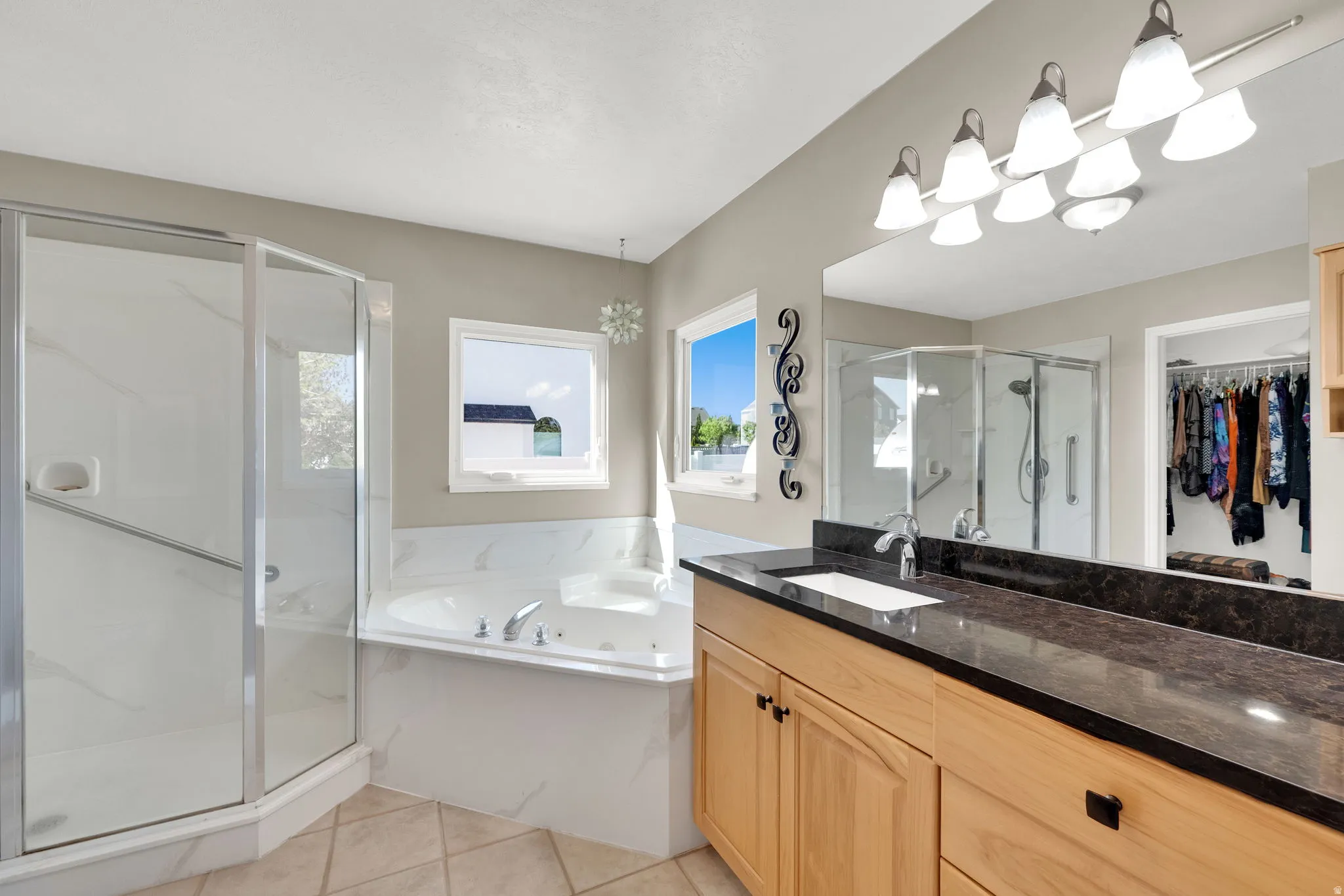 Spacious bathroom featuring a glass-enclosed shower, corner soaking tub, wood-finish vanity with an integrated sink, and a large mirror