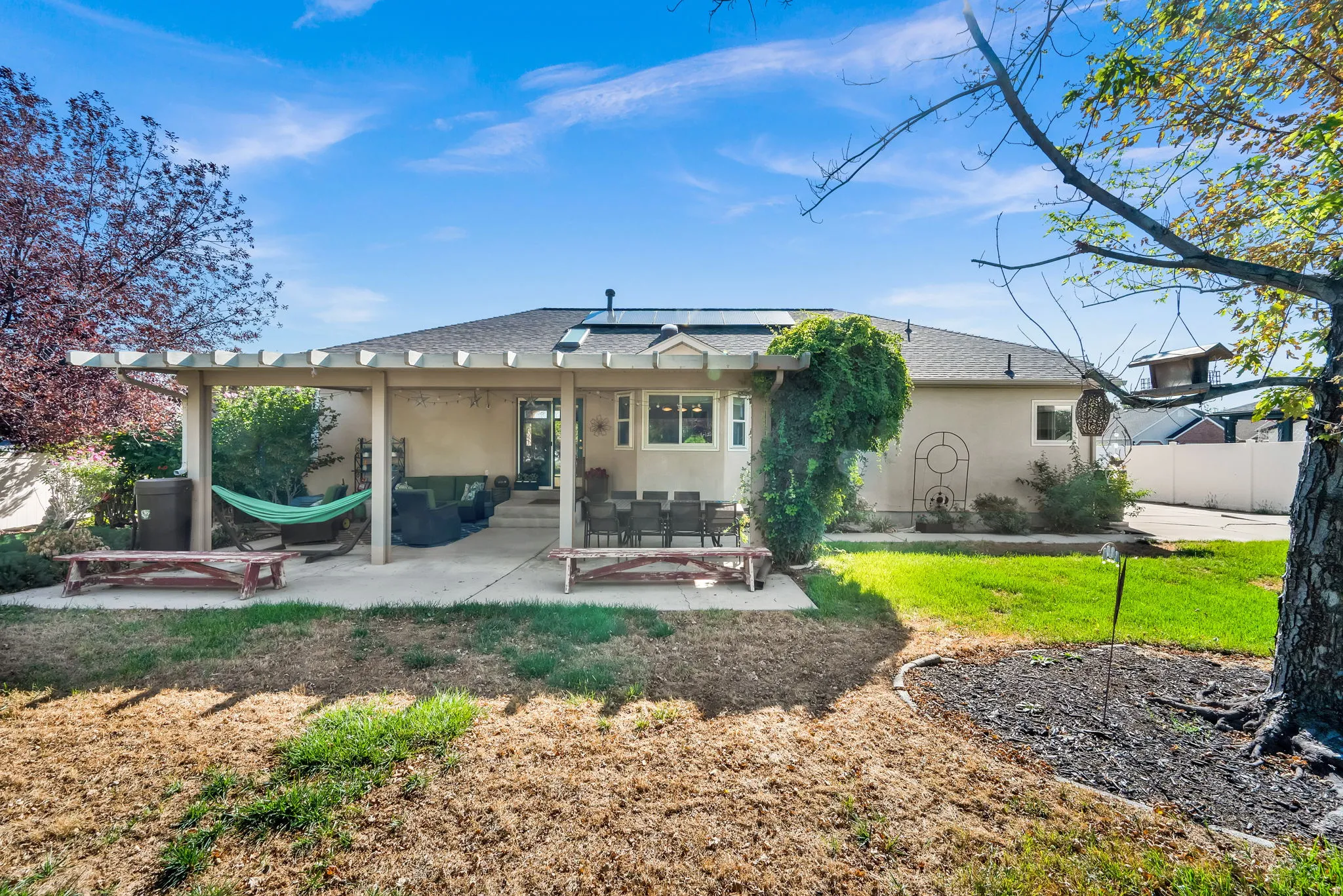 Spacious backyard retreat featuring a covered patio with overhead beams, mature landscaping with established trees, and a level lawn ideal for outdoor entertaining