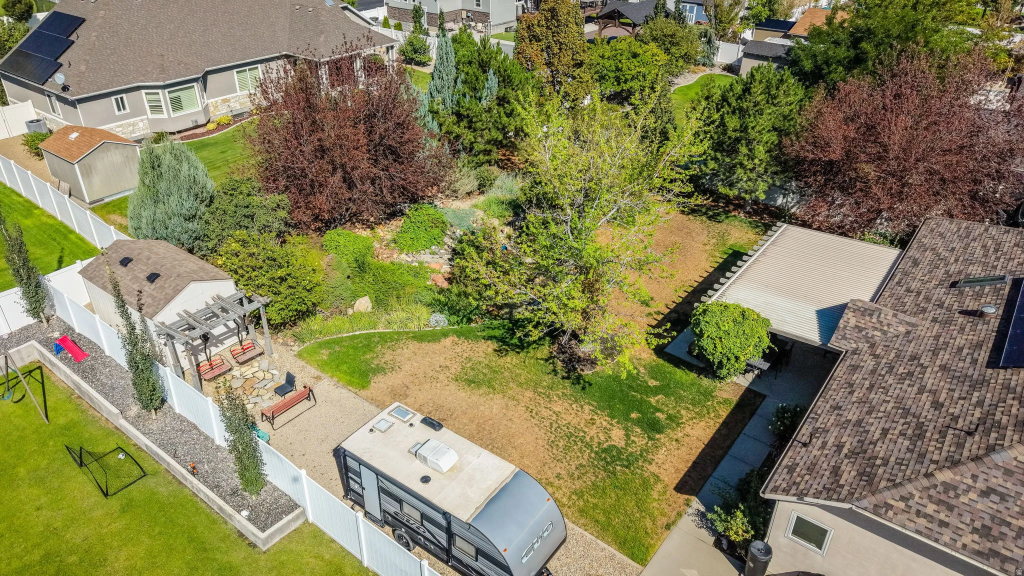 Expansive property featuring a paved driveway, detached storage shed, white privacy fencing, mature trees, and solar panels