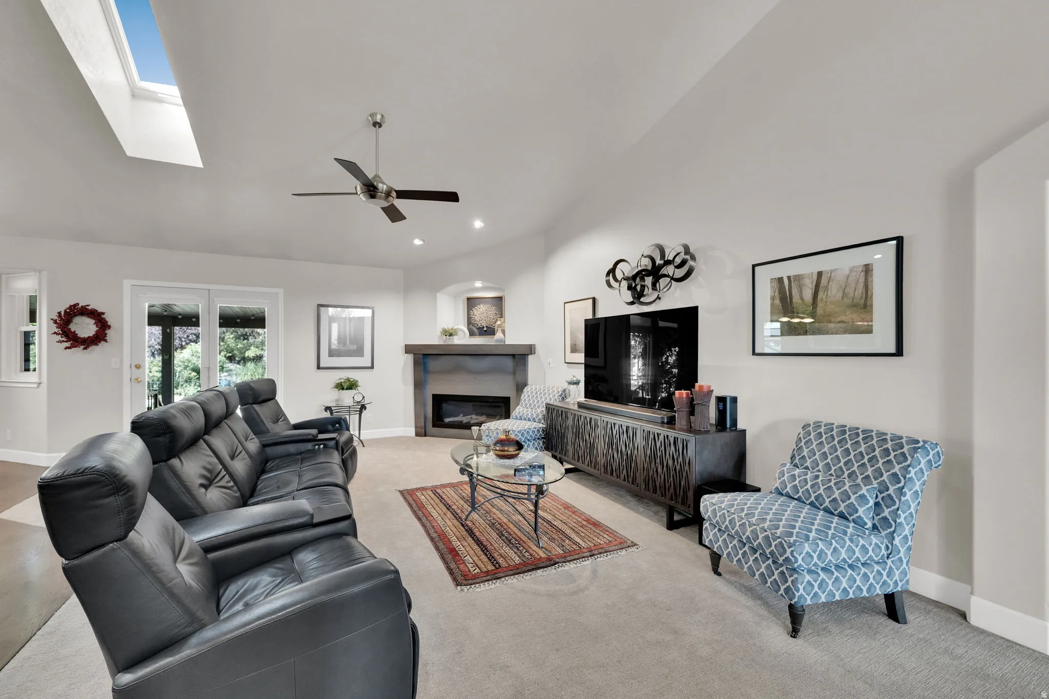 Vaulted ceiling with skylight and ceiling fan, built-in fireplace, recessed lighting, and French doors