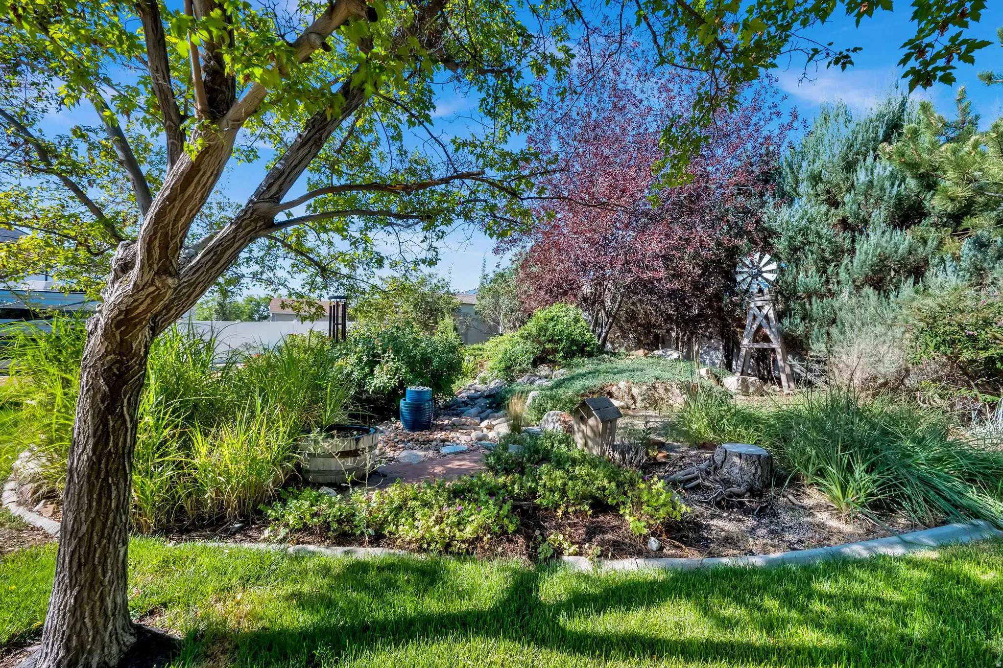 Lush landscaping featuring mature trees, diverse plantings, and a decorative windmill