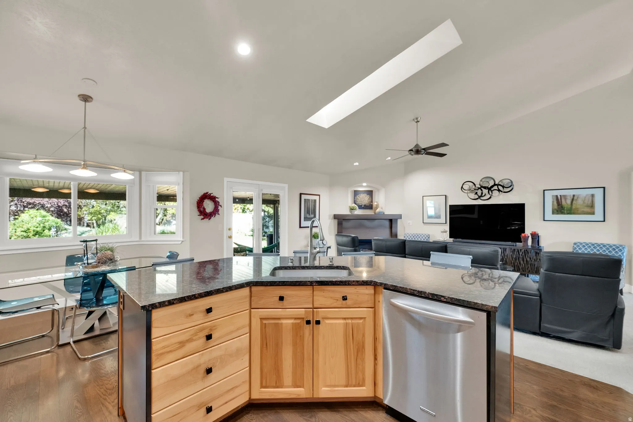 Kitchen island with a built-in stainless steel dishwasher, wood cabinetry with black hardware, and a dark stone countertop