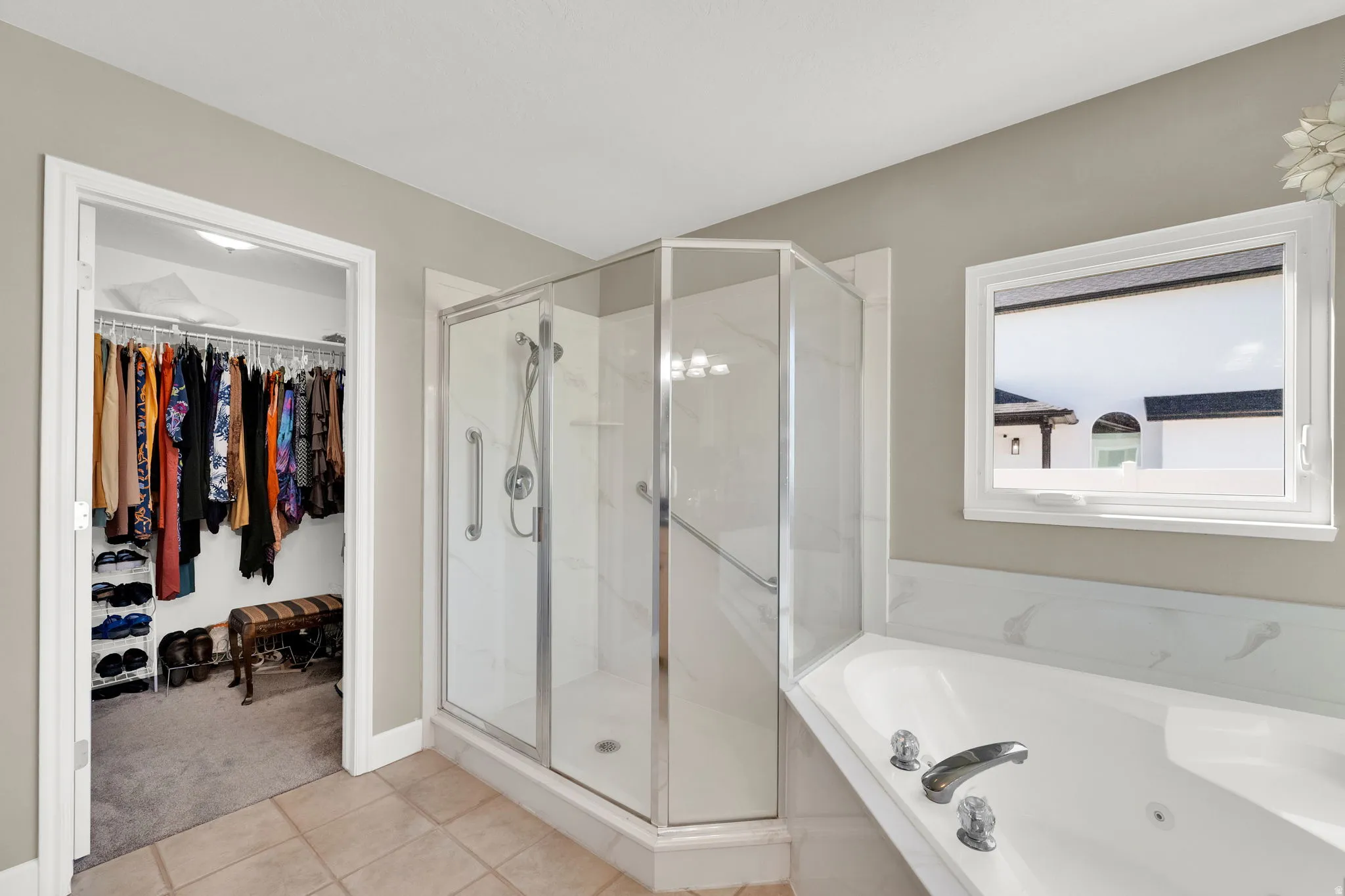 Walk-in closet with built-in shelving, glass-enclosed shower, jetted soaking tub, and a window providing natural light