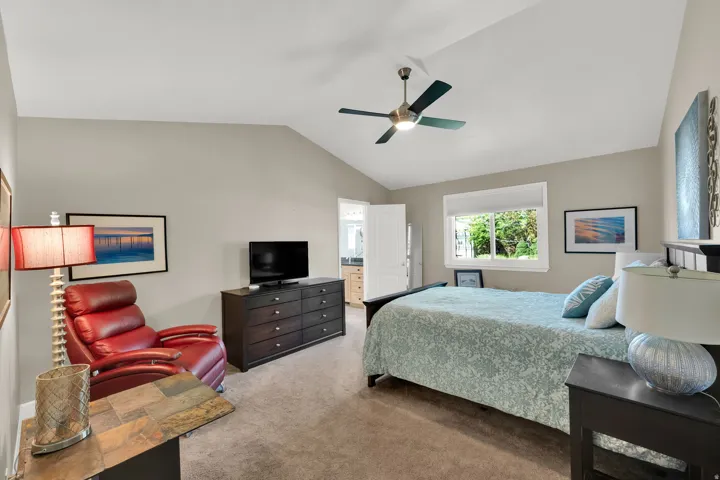 Vaulted ceiling with a ceiling fan, window with roller shade, recessed window, dark wood-finish dresser, and light-tone carpeting