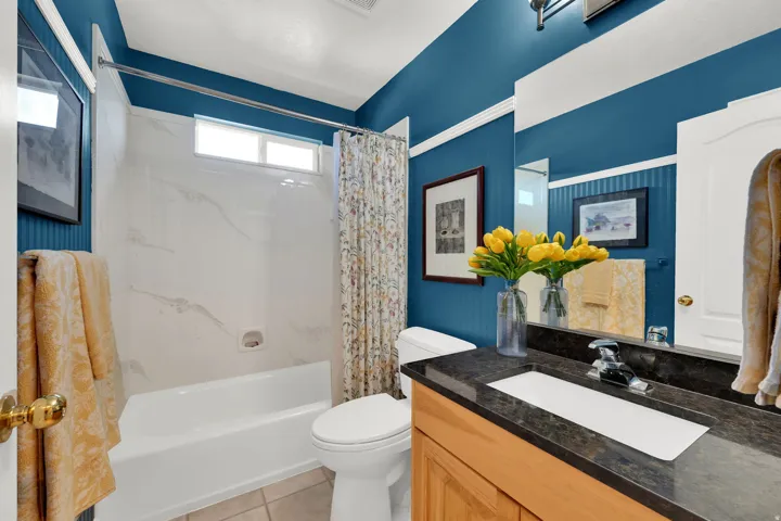 Tub and shower combination with a small window, single vanity with a dark stone countertop, built-in rectangular sink, and tile flooring