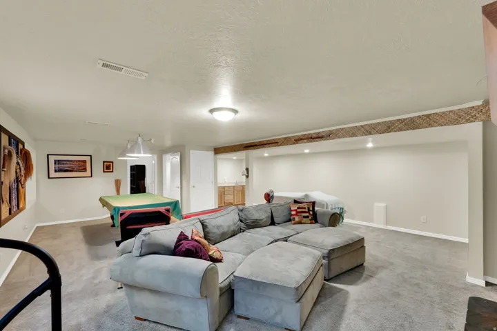 Spacious lower-level area with carpeted flooring, recessed lighting, and a built-in wet bar featuring wood-finish cabinetry