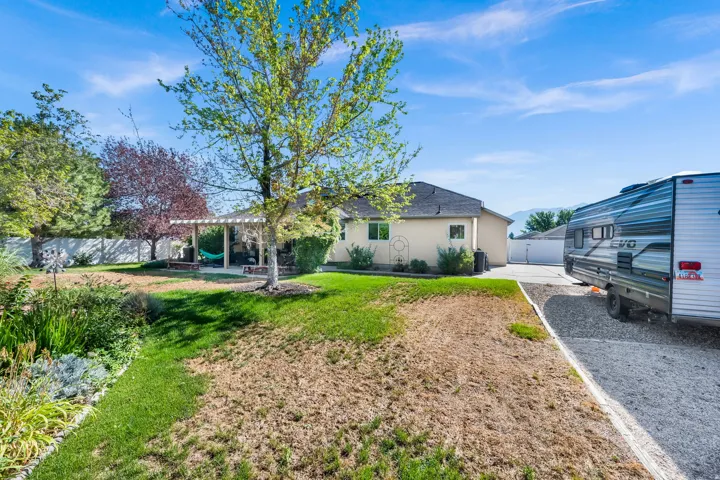 Expansive backyard with a covered patio, mature trees, and a white privacy fence