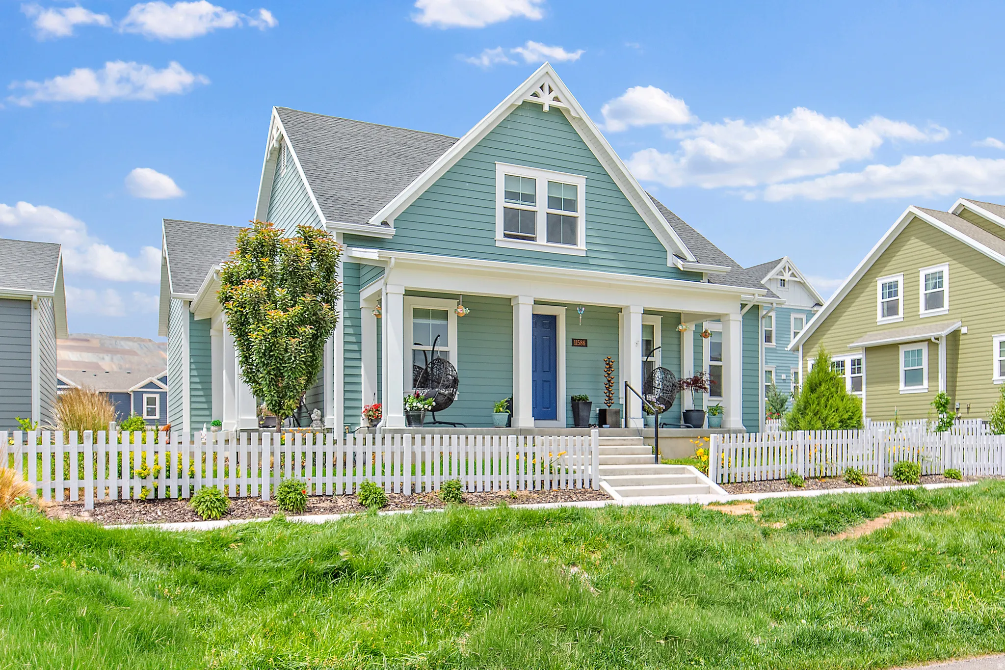 Charming farmhouse-style home featuring a light green exterior with white trim, gabled roofline, and covered front porch