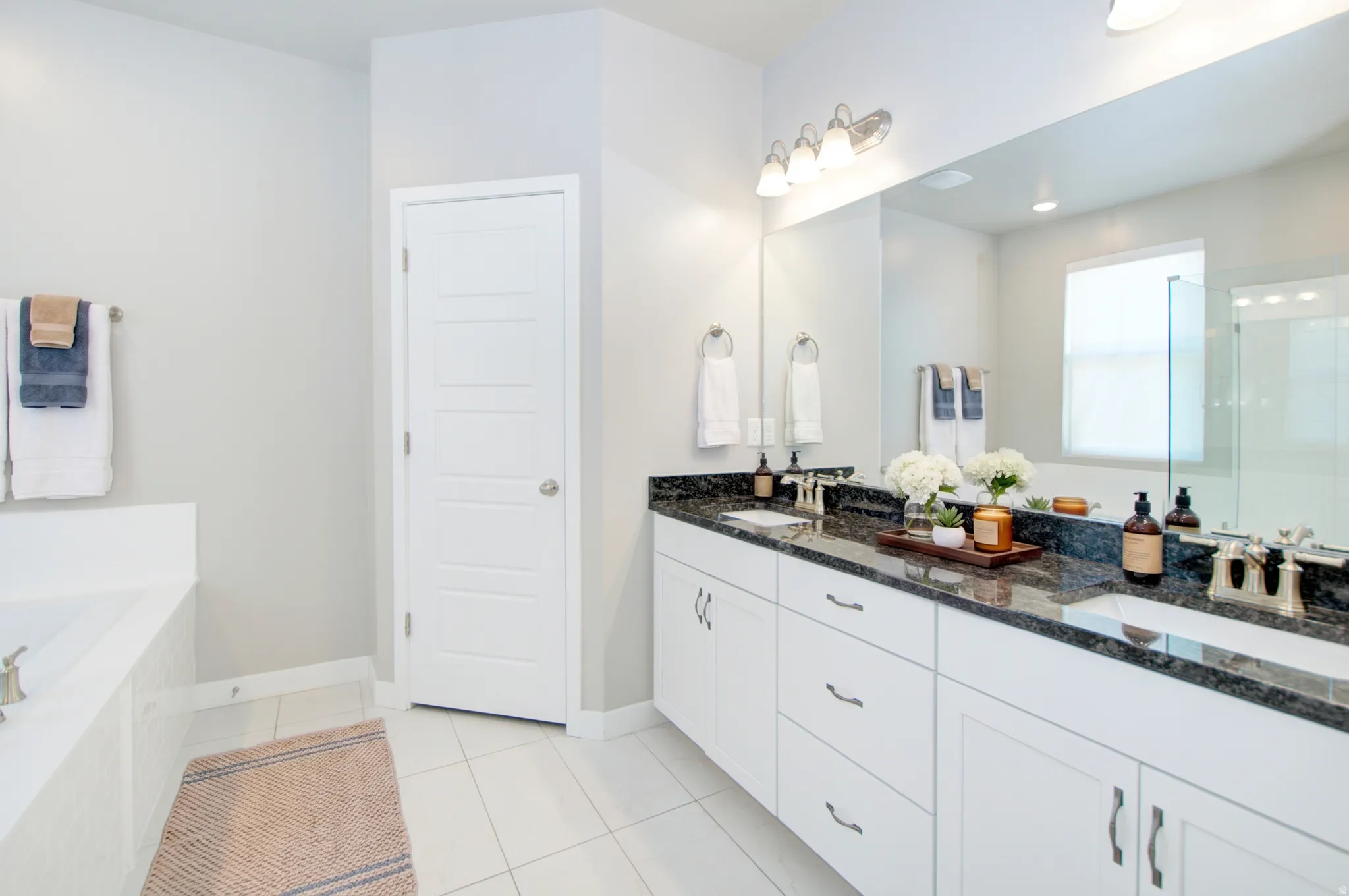 Dual vanity with dark stone countertop, undermount sinks, and white cabinetry