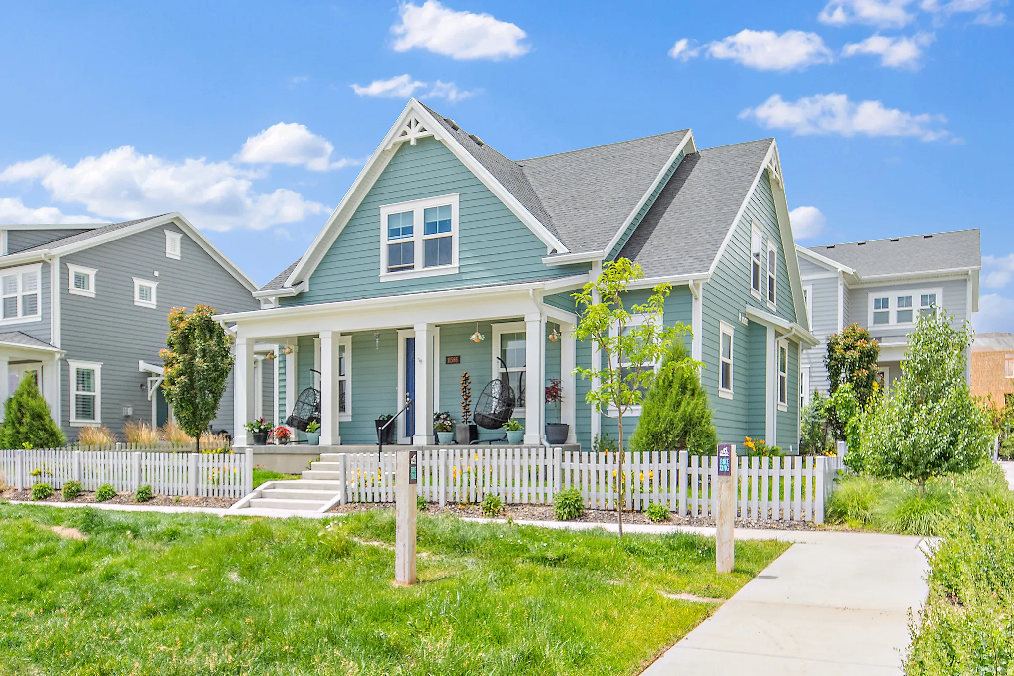 Charming farmhouse-style home featuring a light blue-green exterior with white trim, gabled roofline, and a full-width front porch with white picket railing
