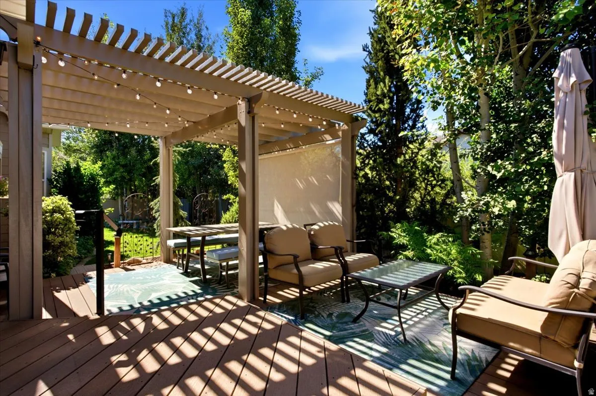 The custom backyard retreat features a large deck with a pergola cover, patio lighting, and mature trees.