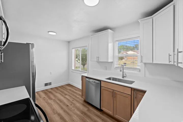 Stainless steel appliances, white countertops, wood-finish flooring, white upper cabinetry, and natural wood-tone lower cabinetry