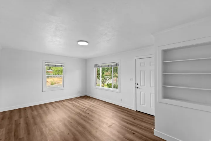 Wood-finish flooring, white walls, two windows, recessed built-in shelving, and a paneled entry door