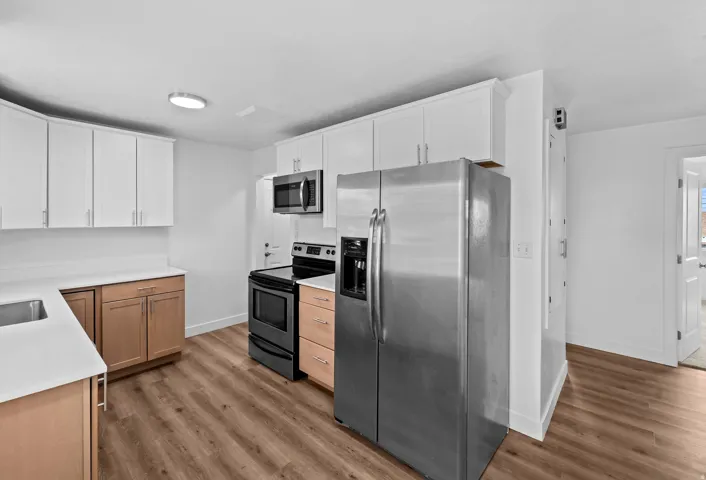 Modern kitchen featuring white upper cabinetry, light wood-finish lower cabinetry, light countertops, and stainless steel appliances