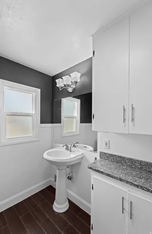 White pedestal sink with chrome faucet, wood-finish flooring, white cabinetry with silver hardware, and a speckled countertop