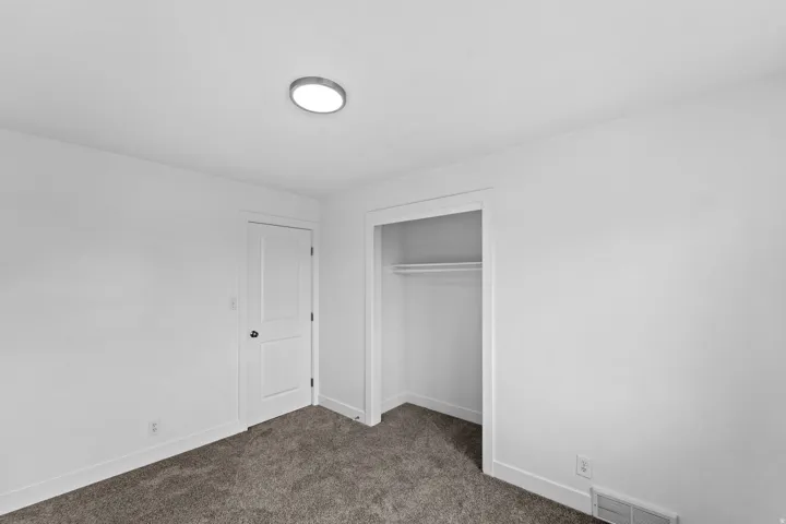 White walls, carpet flooring, a single overhead light fixture, and a built-in closet with a hanging rod