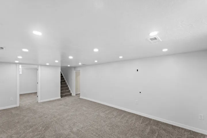 Recessed lighting, light gray carpeting, white painted walls, white trim, and a carpeted staircase