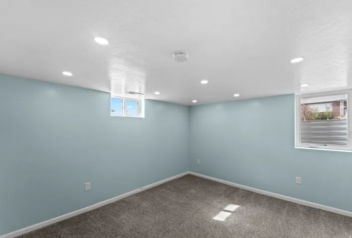 Recessed lighting illuminating the space, light blue painted walls, and textured carpeting