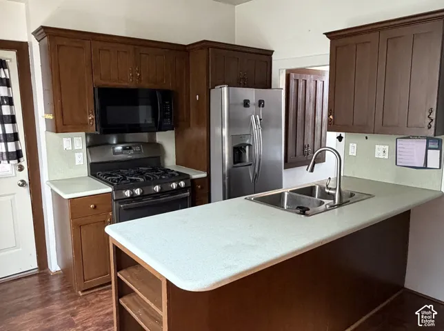 Kitchen featuring wood-finish cabinetry, light-toned countertops, and a stainless steel double basin sink with a gooseneck faucet