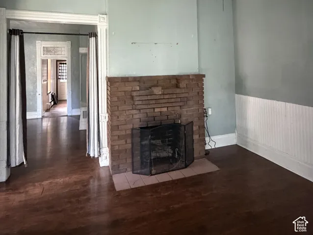 Brick-clad fireplace with a tile hearth, hard-surface flooring, and wainscoting