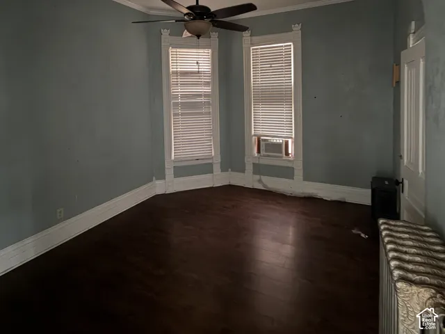 Wood-finish flooring with white trim, two windows with blinds, a ceiling fan, and a paneled door