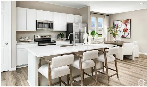 White cabinetry, stainless steel appliances, central island with seating, wood-finish flooring, and a dining area with a large window
