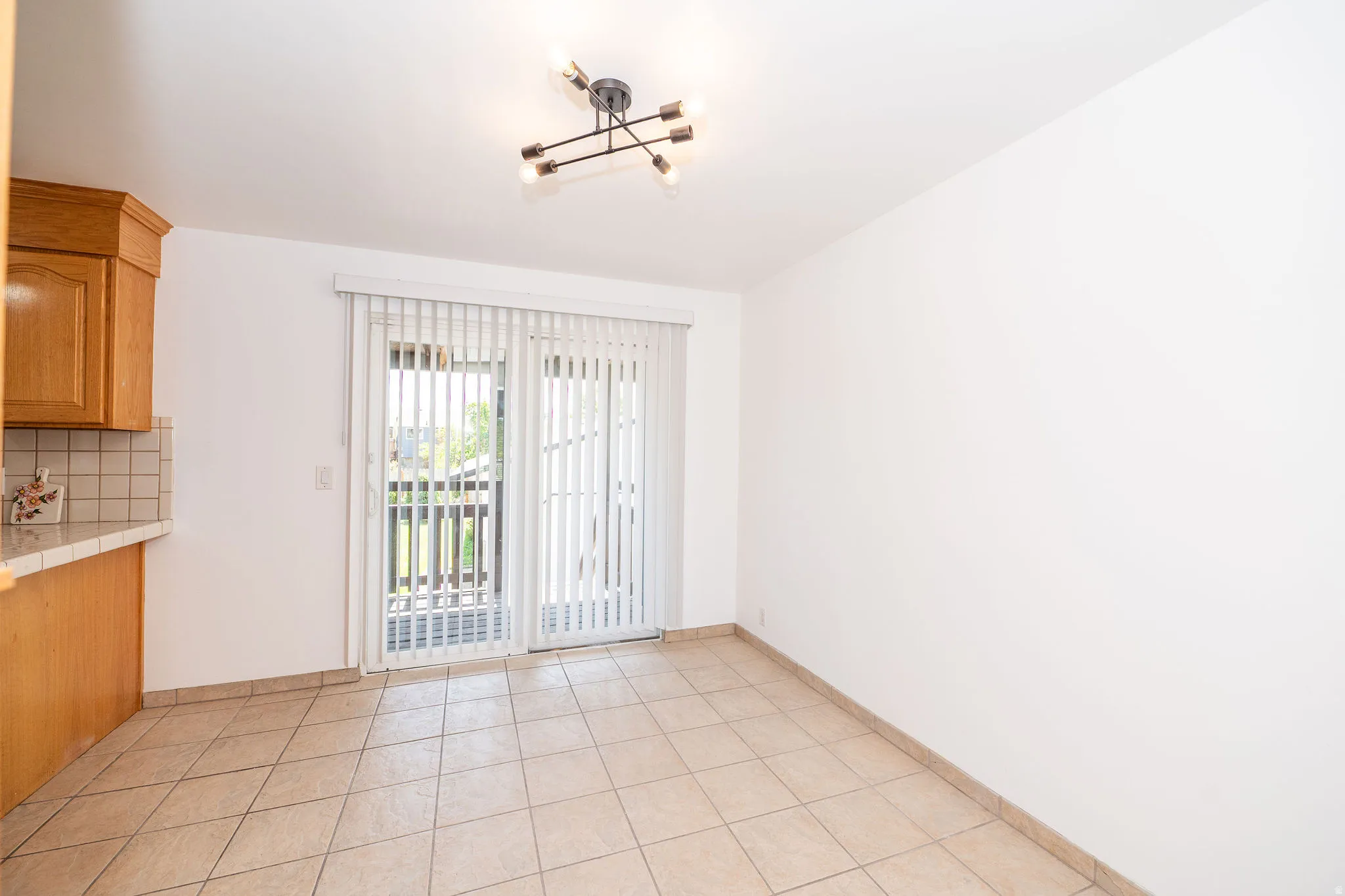 Recessed lighting fixture, light wood cabinetry, tiled backsplash, tile flooring, and sliding glass door