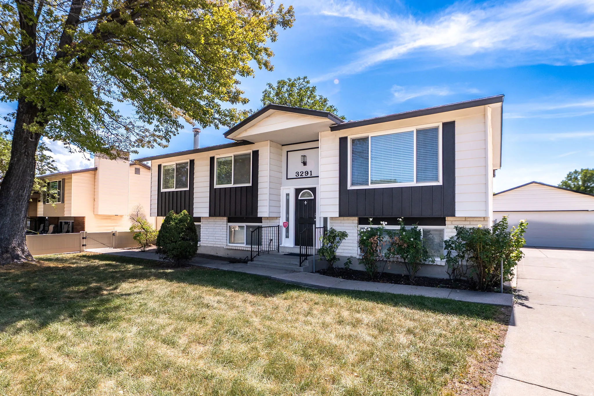 Split-level exterior featuring white siding, black trim, a prominent front door, and an attached garage with a driveway