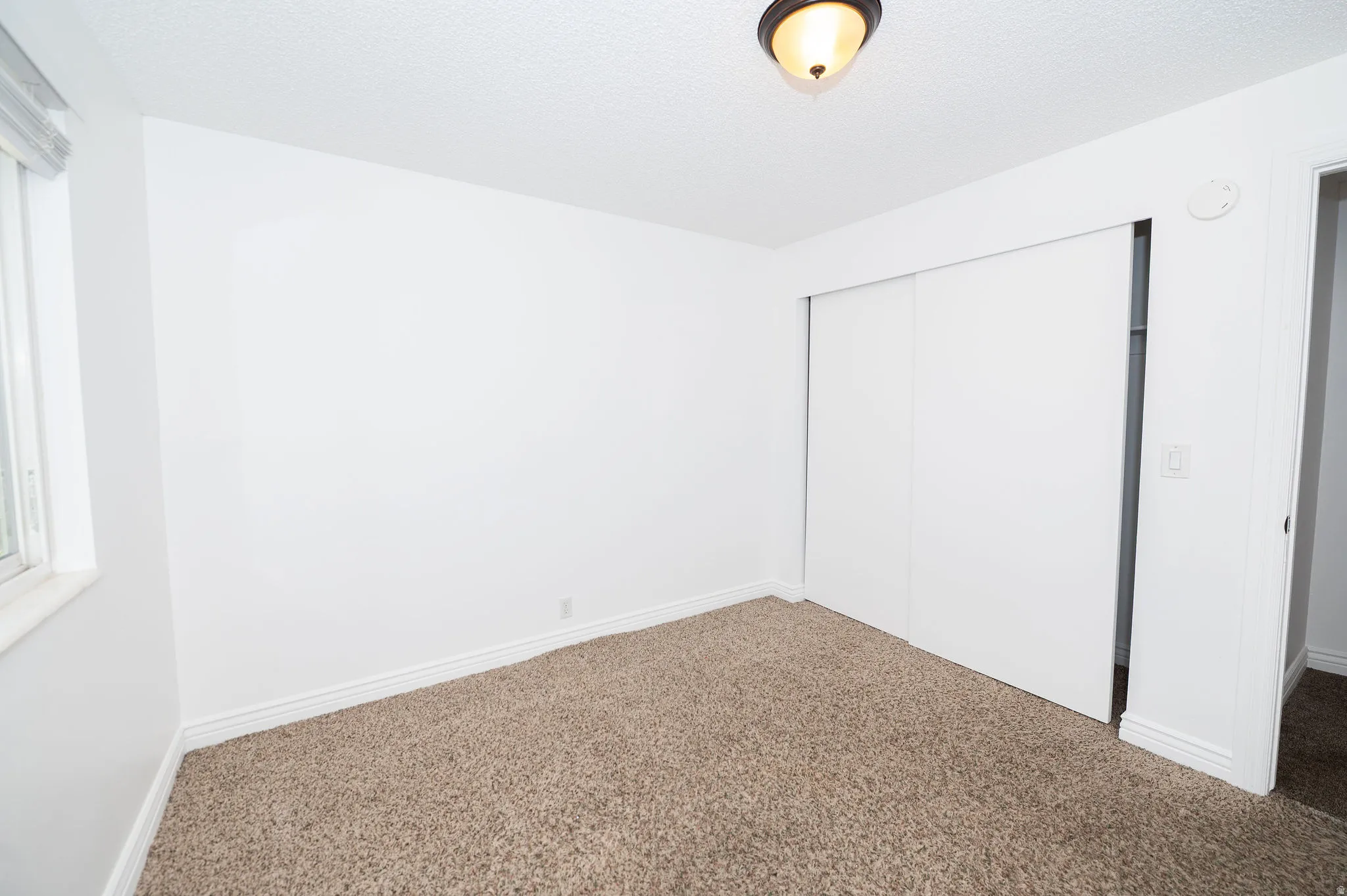 Wall-to-wall carpeting, window with blinds, bi-fold closet doors, and overhead light fixture
