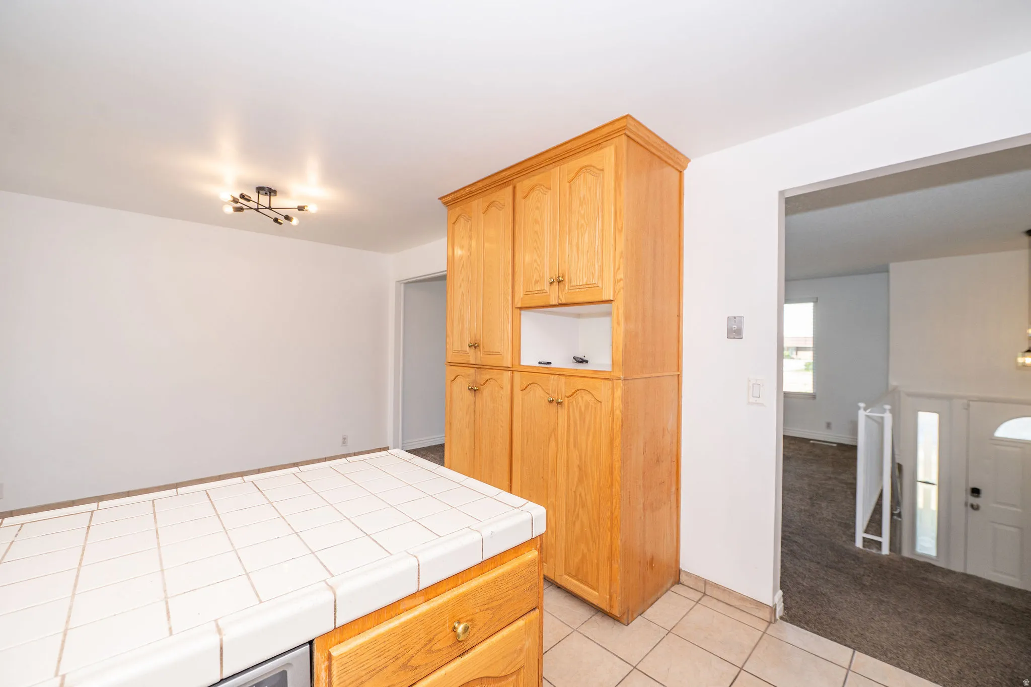 Wood-finish cabinetry, tile flooring, tile countertop, and a modern ceiling light fixture