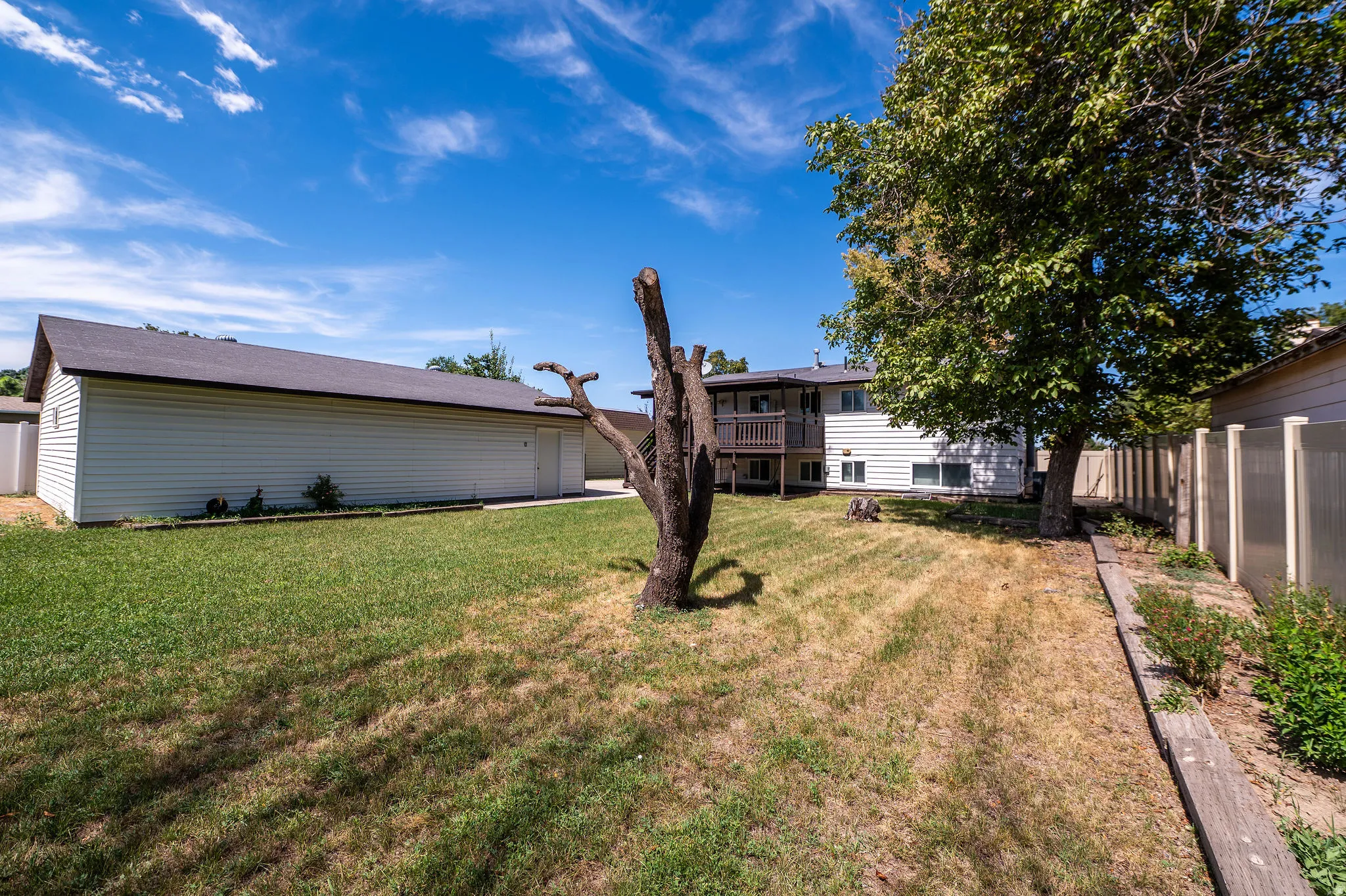 Expansive backyard featuring a large detached garage with shingled roofing, a multi-level deck, and a privacy fence