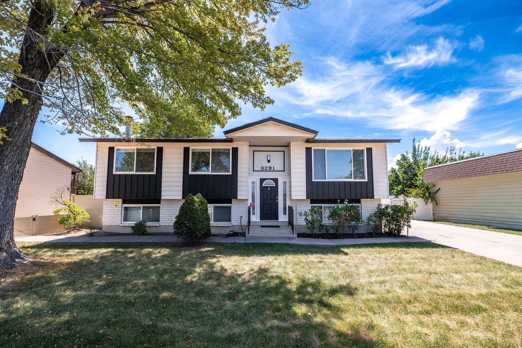 Split-level residence featuring a white and black exterior, front entry with transom window, and an attached garage