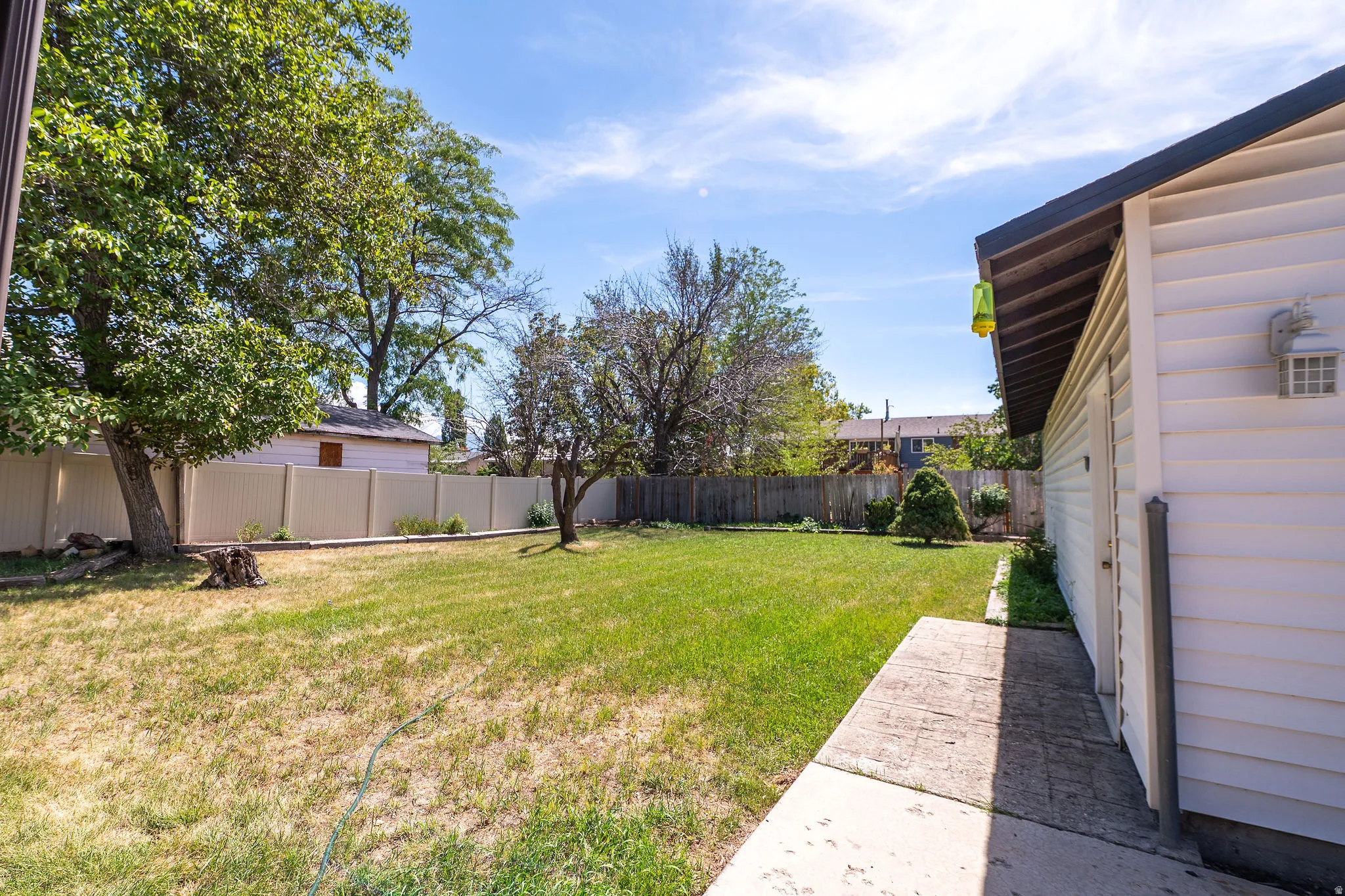 Expansive lawn area with mature trees, vinyl privacy fencing, and a concrete pathway