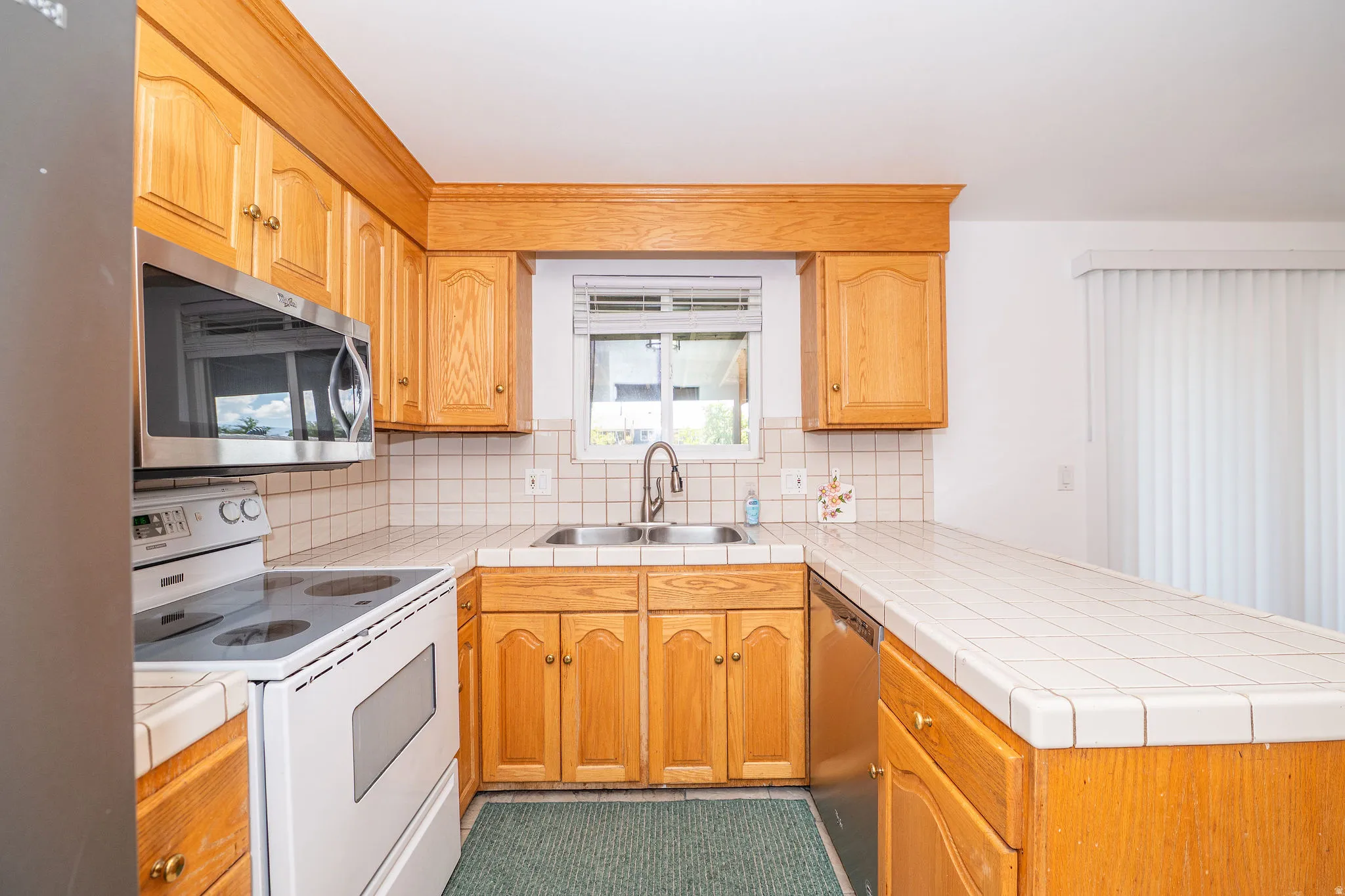 Kitchen featuring wood cabinetry, tile countertops, tile backsplash, built-in microwave, and stainless steel sink