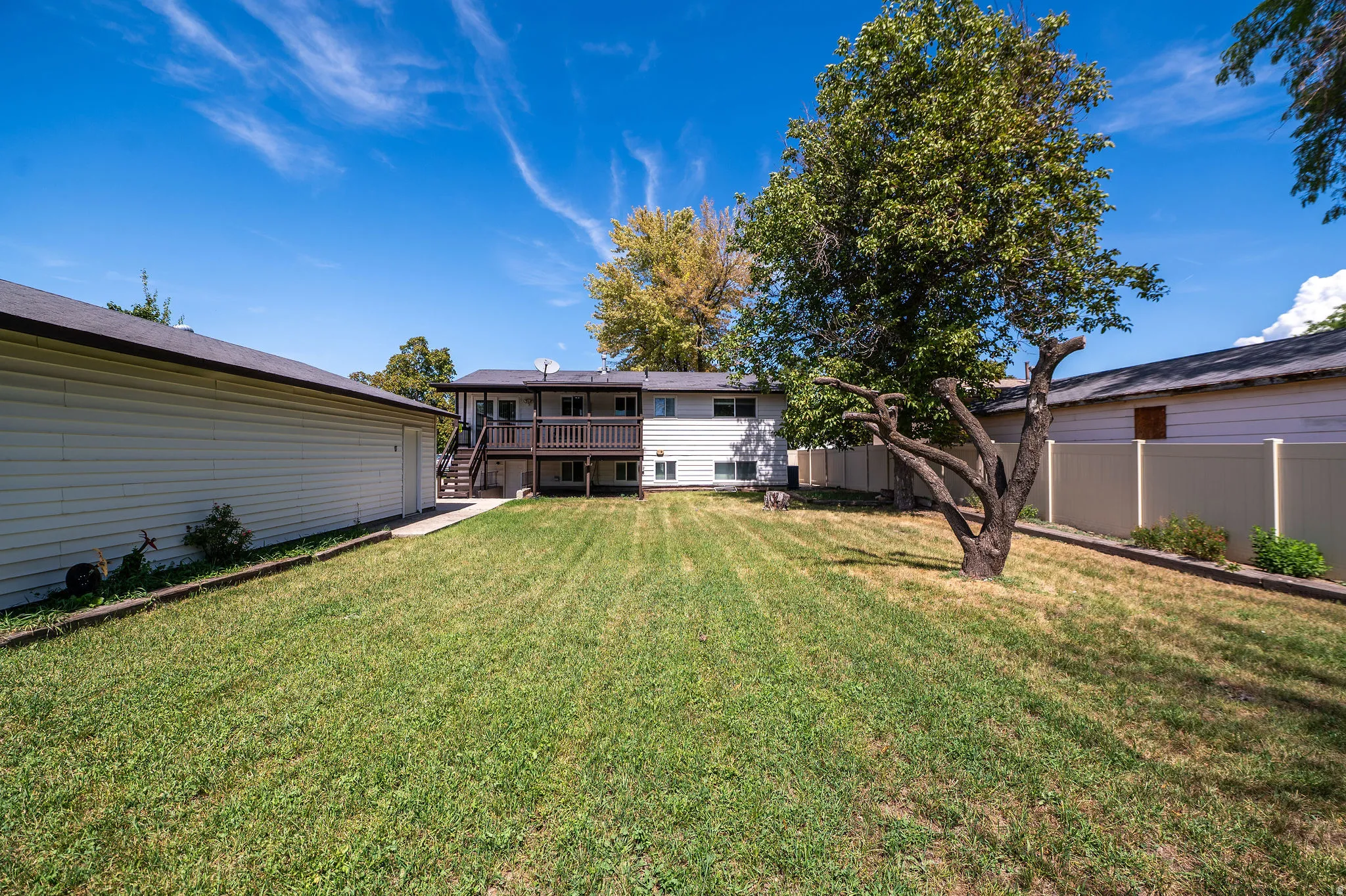 Expansive grassy yard with mature trees, a two-story residence featuring a wood-decked balcony, and a detached auxiliary structure