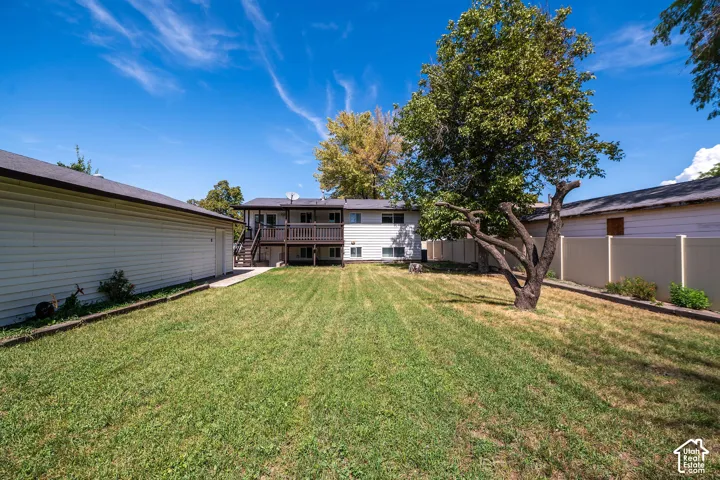 Expansive grassy yard with mature trees, a two-story residence featuring a wood-decked balcony, and a detached auxiliary structure