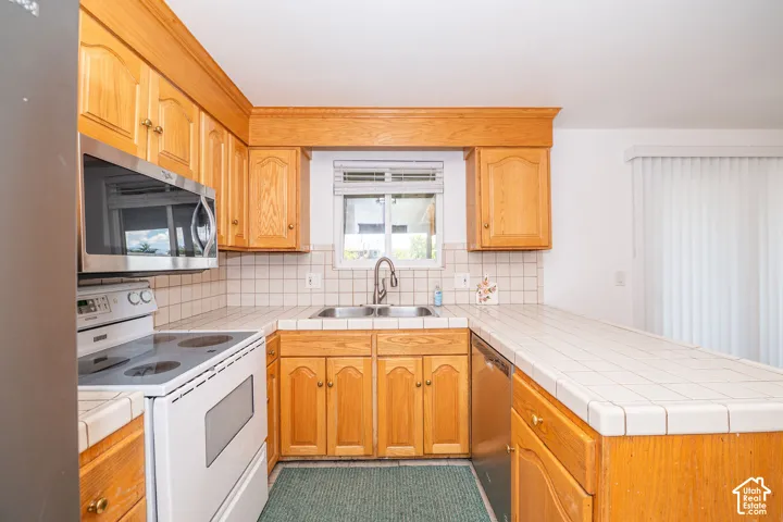 Kitchen featuring wood cabinetry, tile countertops, tile backsplash, built-in microwave, and stainless steel sink
