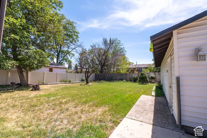 Expansive lawn area with mature trees, vinyl privacy fencing, and a concrete pathway