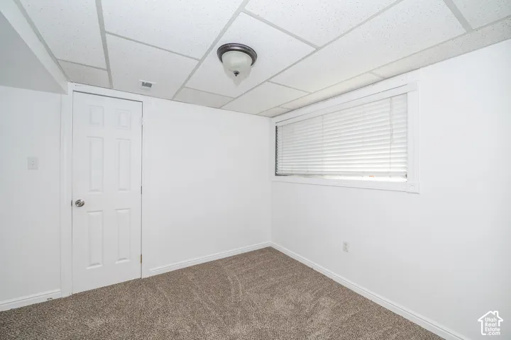 White painted walls, drop ceiling, flush mount light fixture, six-panel interior door, and window with white blinds