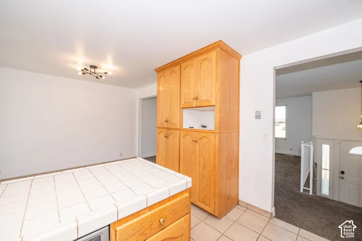 Wood-finish cabinetry, tile flooring, tile countertop, and a modern ceiling light fixture