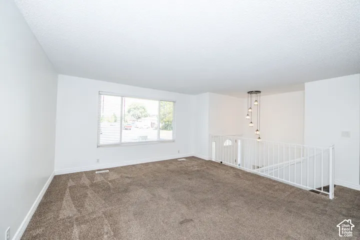 White walls, brown carpet, window with horizontal blinds, white railing, and a multi-pendant light fixture