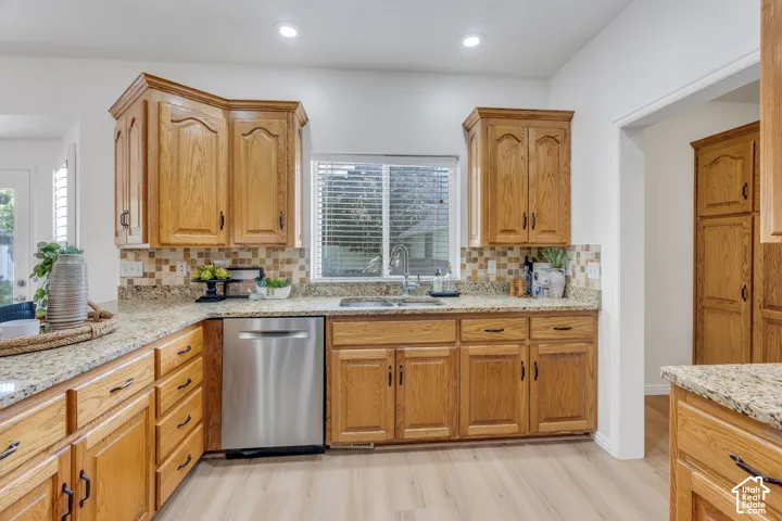 Kitchen featuring granite countertops, wood cabinetry, stainless steel dishwasher, mosaic tile backsplash, and wood-finish flooring