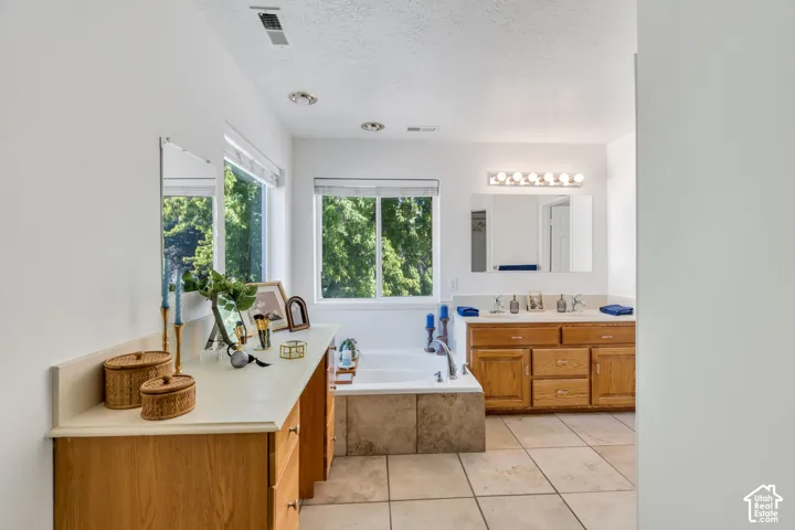 Dual wood-finish vanities with light-toned countertops, an integrated soaking tub, and tile flooring