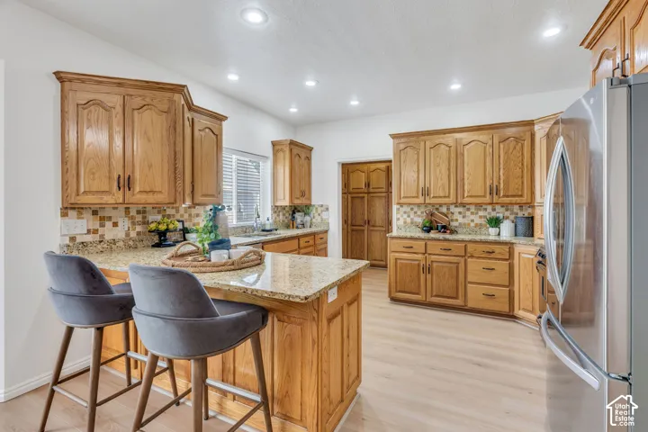 Kitchen featuring wood cabinetry, granite countertops, tile backsplash, stainless steel refrigerator, and light wood-finish flooring