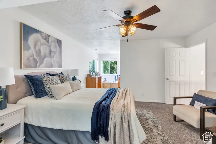 White painted walls, textured ceiling, brown wood-finish ceiling fan with decorative light fixture, carpeted flooring, and white interior door